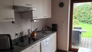 Une cuisine moderne avec des meubles blancs, un plan de travail noir et un lave-vaisselle. Une fenêtre offre une vue sur un jardin et une terrasse à l  ’extérieur.