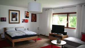 Une chambre moderne avec un lit en bois, une télévision, un canapé et des œuvres d’art accrochées aux murs.