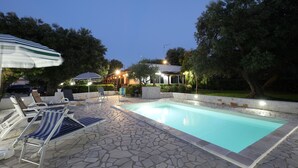 A swimming pool with lounge chairs and umbrellas, surrounded by stone tiles and greenery.