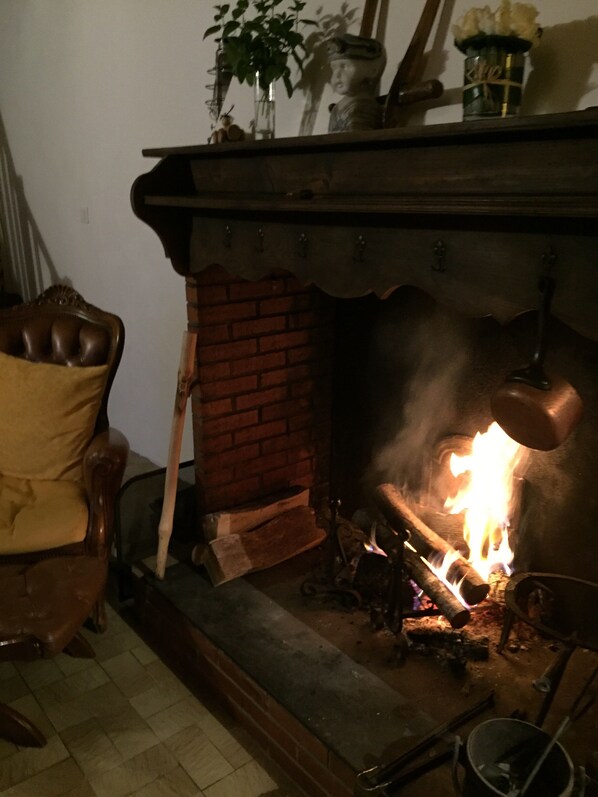 A fireplace with burning logs, a brick wall, and a wooden chair. - Gîte de l'arac, Comfortable house with fireplace. Mountain view, (Massat)