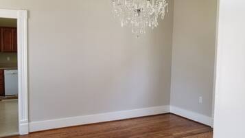 A spacious room with hardwood flooring, a chandelier, and a kitchen visible through an open doorway.