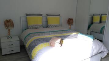 Una cama bien tendida con una colcha estampada, dos mesitas de noche con lámparas, y un espejo en la pared.