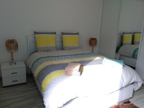 A neatly made bed with a patterned bedspread, two bedside tables with lamps, and a mirror on the wall.