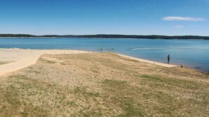 A beach with a clear sky, calm water, and a person standing by the water's edge. - LAKE ACCESS & GREAT VIEWS! MINUTES TO THE WHITE RIVER!! 3 BR/2BA, 1500 sq. ft. (Bull Shoals)