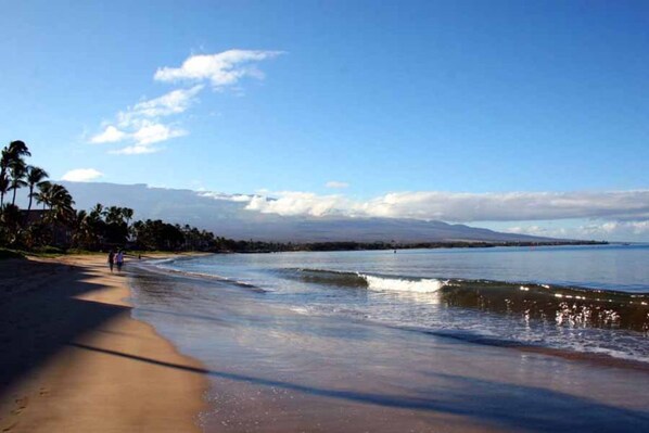 Une plage avec un ciel dégagé, une eau calme et une chaîne de montagnes à l’horizon.