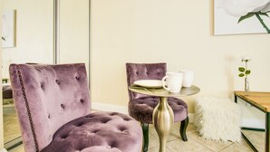A room with a tufted purple chair, a small round table with a white mug and plate, and a white fluffy ottoman. - Queen Studio, Full Kitchen 1.5 mins from the Beach (Honolulu)