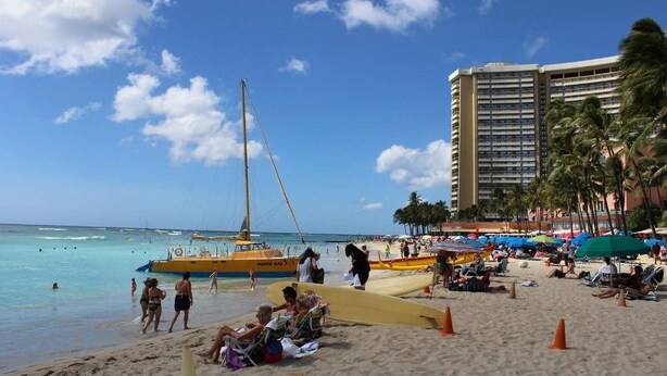 A beach with a yellow boat, people sunbathing, and a tall hotel in the background. - Queen Studio, Full Kitchen 1.5 mins from the Beach (Honolulu)
