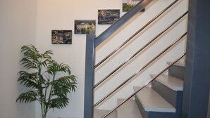 Un escalier avec des rampes en métal et des marches blanches, une plante en pot et des tableaux encadrés accrochés au mur.