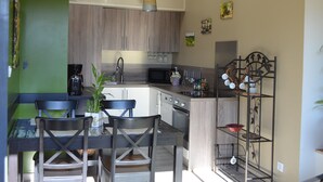 Une cuisine moderne avec des meubles en bois, un coin repas comprenant une table et des chaises, et une étagère en métal où sont rangés de la vaisselle.