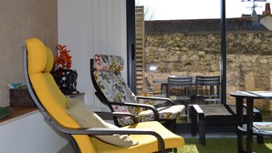 Une terrasse ensoleillée avec une chaise jaune, une chaise à motifs floraux et une petite table entourée de chaises.