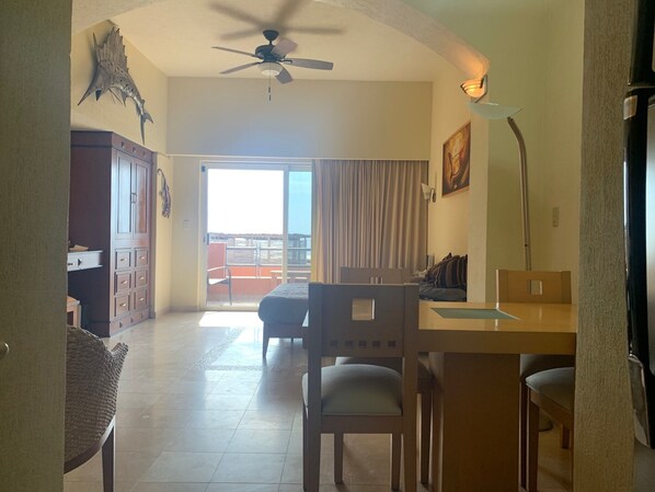 A hotel room with a balcony, a dining area, and a ceiling fan.