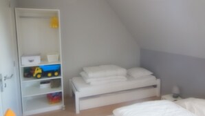 A bedroom with a bed, a nightstand, a shelf with toys, and a hanging light fixture. - The Becots, family villa near beach with garden (Neufchâtel-Hardelot)