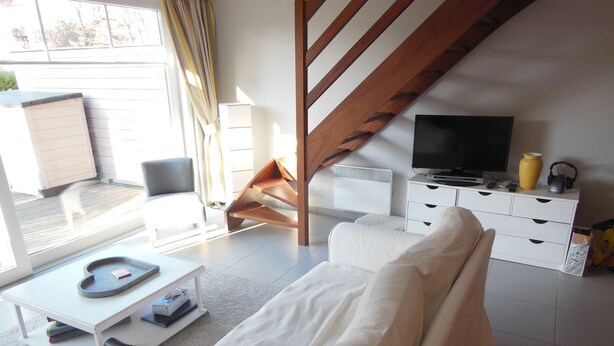 A modern living room with a white sofa, a coffee table, a TV, and a staircase. - The Becots, family villa near beach with garden (Neufchâtel-Hardelot)