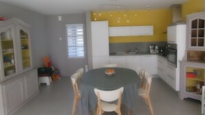 A compact kitchen with white cabinets, a dining table with chairs, and a yellow accent wall. - The Becots, family villa near beach with garden (Neufchâtel-Hardelot)
