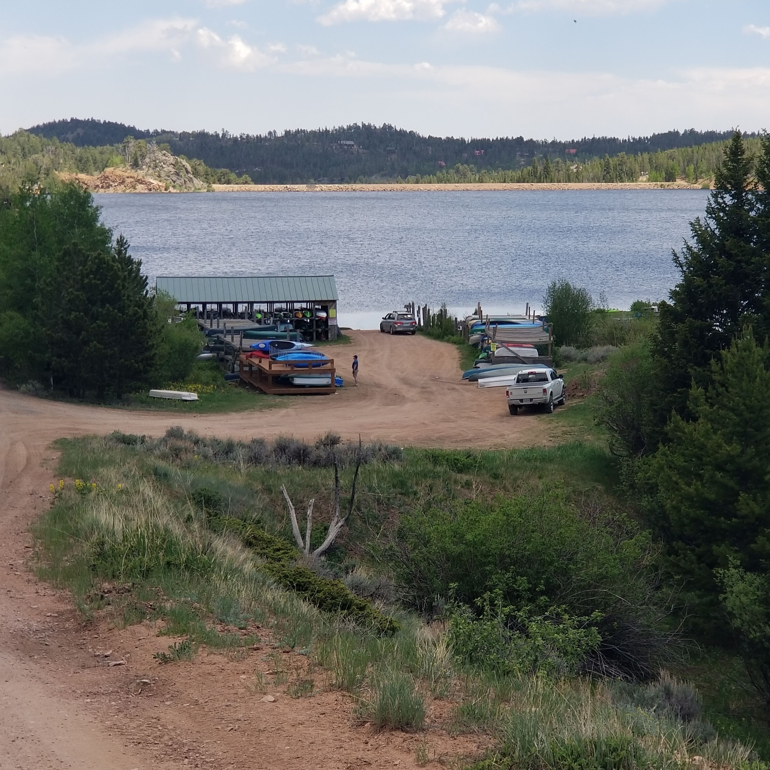 A lakeside area with a dock and boats, surrounded by trees and a distant hill.