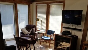 Ett vardagsrum med trägolv, en gungstol, en soffa, en tv och ett litet bord.