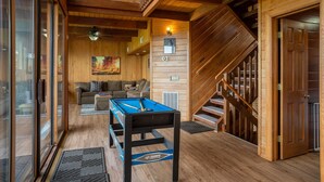 A cozy room with a pool table, wooden walls, a staircase, and a sofa.