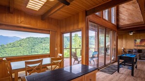 A wooden interior with a pool table, dining area, and large windows offering a mountain view.