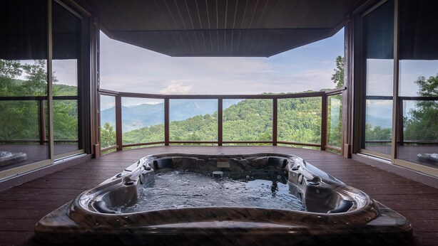 A hot tub in a room with large windows overlooking a mountainous landscape.
