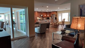 A spacious living area with a glass sliding door leading to a patio, a kitchen with wooden cabinets, and a ceiling fan. - Vacation Pool Home - On 200ft Wide, Sailboat access Canal - SE Cape Coral! (Cape Coral)