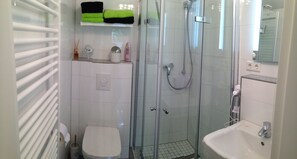 A modern bathroom with a glass shower enclosure, a toilet, a sink, and a towel rack with folded towels. - small cozy, lovingly furnished holiday house for 2 people (Dresden)