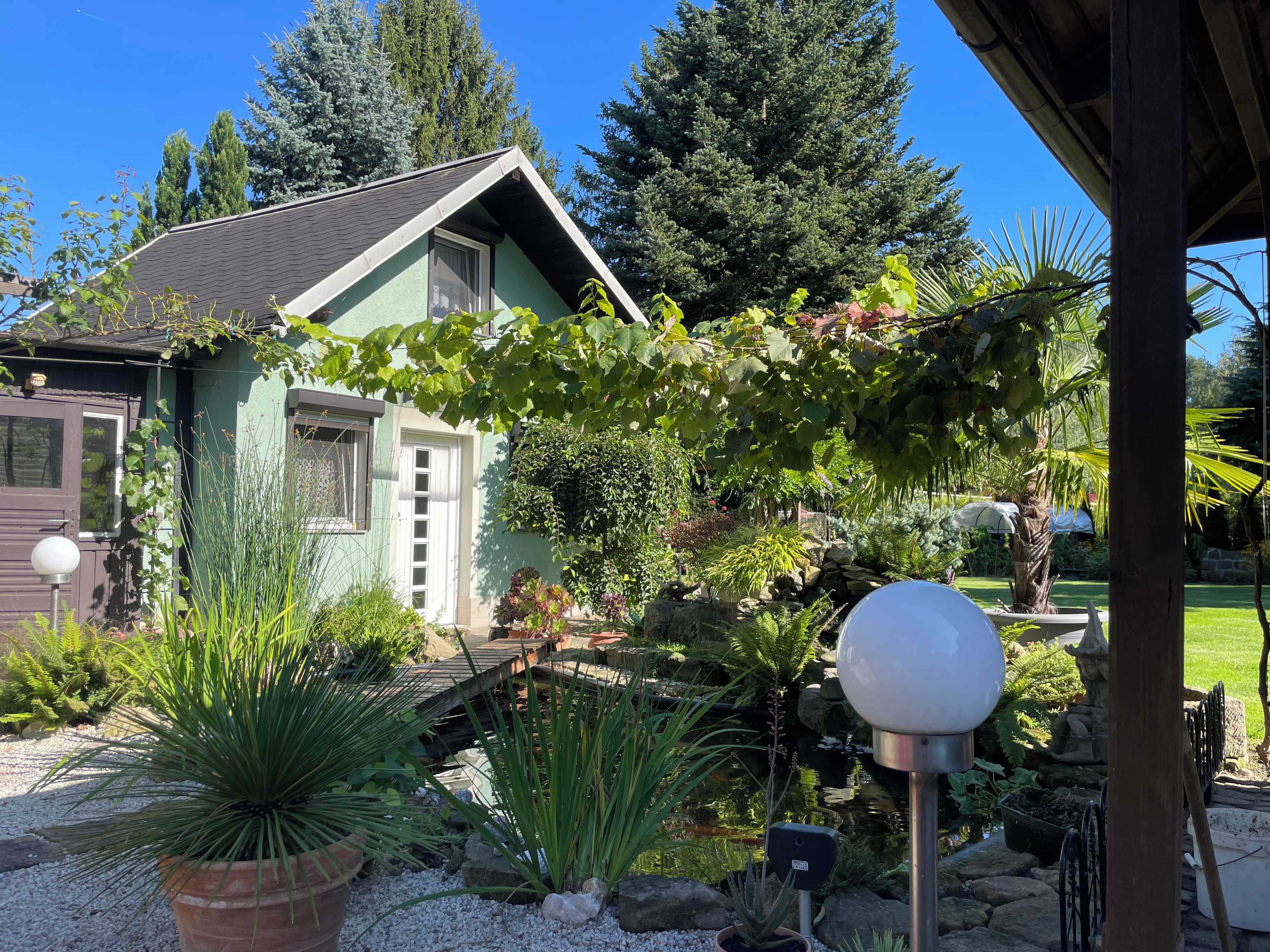 A house with a green exterior, a wooden deck, and a garden with various plants and a small pond.
