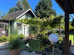 A house with a green exterior, a wooden deck, and a garden with various plants and a small pond. - small cozy, lovingly furnished holiday house for 2 people (Dresden)