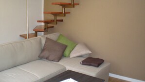 A living room with a beige sofa, a coffee table, and a wooden floating staircase. - small cozy, lovingly furnished holiday house for 2 people (Dresden)
