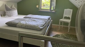 Un dormitorio con una cama, dos almohadas, una silla, un ventanal y un ventilador de techo.