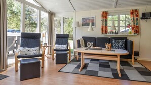A modern living room with a sofa, two armchairs, a coffee table, and a TV. Large windows provide natural light and a view of the outdoors. - Beautiful home in Ringkøbing with sauna (Ringkøbing)