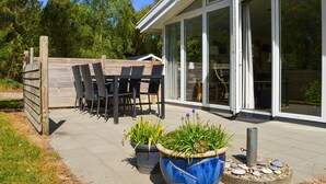 An outdoor patio with a wooden table and chairs, potted plants, and a stone feature. - Beautiful home in Ringkøbing with sauna (Ringkøbing)