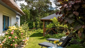 Un jardin agrémenté d’un kiosque, d’une table avec des chaises et d’une maison à toit de chaume.