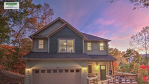 A two-story house with a garage, a deck, and a view of trees.