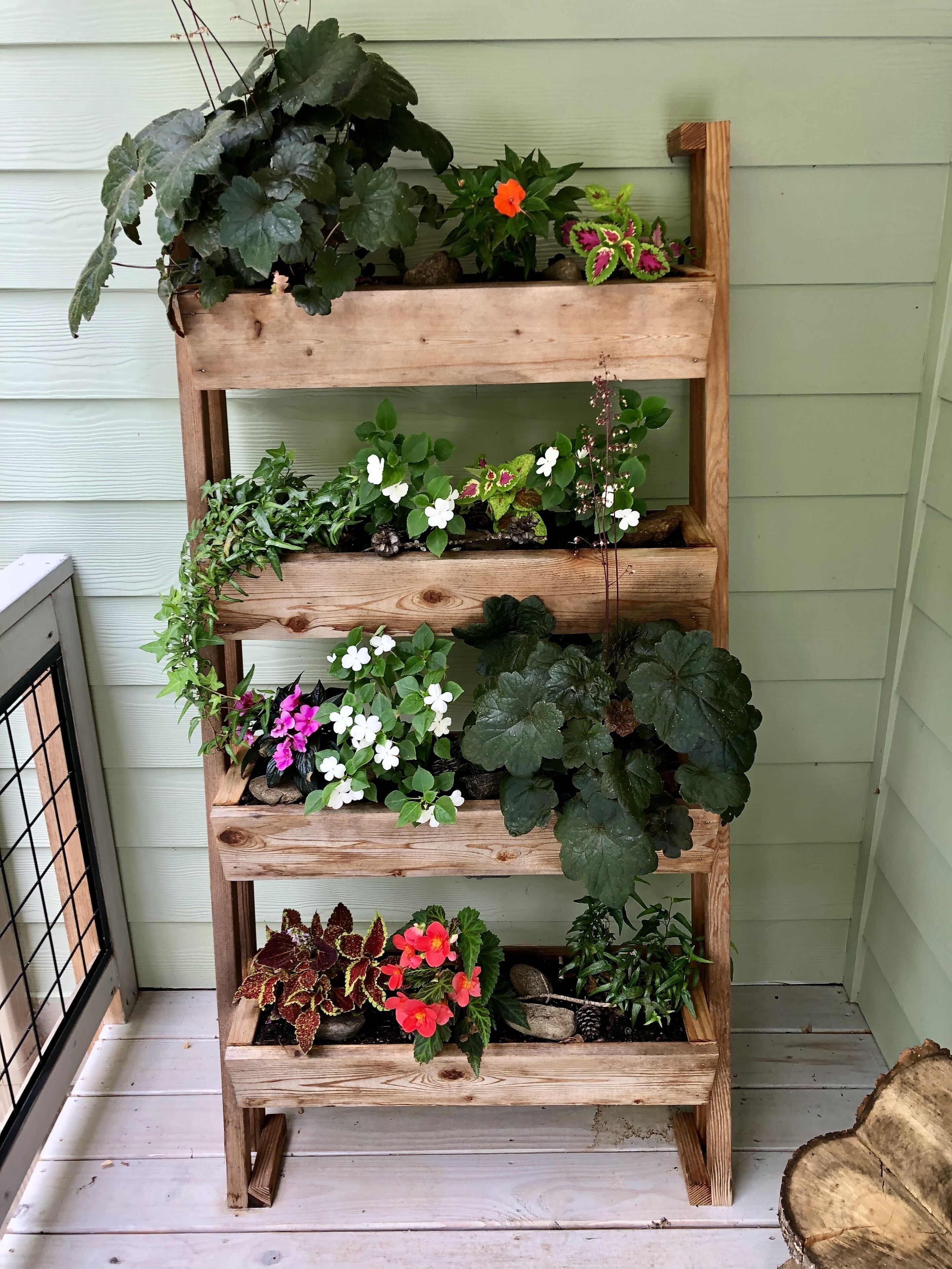 A wooden tiered plant stand with various potted plants and flowers.