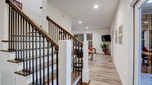 A modern interior with a wooden staircase, a dining area with a table and chairs, and a large window providing natural light.
