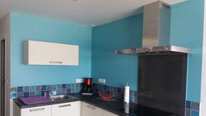 A modern kitchen with blue walls, a black countertop, and white cabinets. - LES PIEDS DANS L'EAU sea at 15 meters PANORAMIC VIEW PERROS GUIREC (PERROS GUIREC)