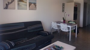 A modern living room with a black sofa, a coffee table with books, and a dining area with a white table and chairs. - LES PIEDS DANS L'EAU sea at 15 meters PANORAMIC VIEW PERROS GUIREC (PERROS GUIREC)
