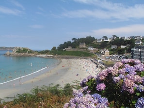 A beach with people, a clear sky, and buildings in the background.