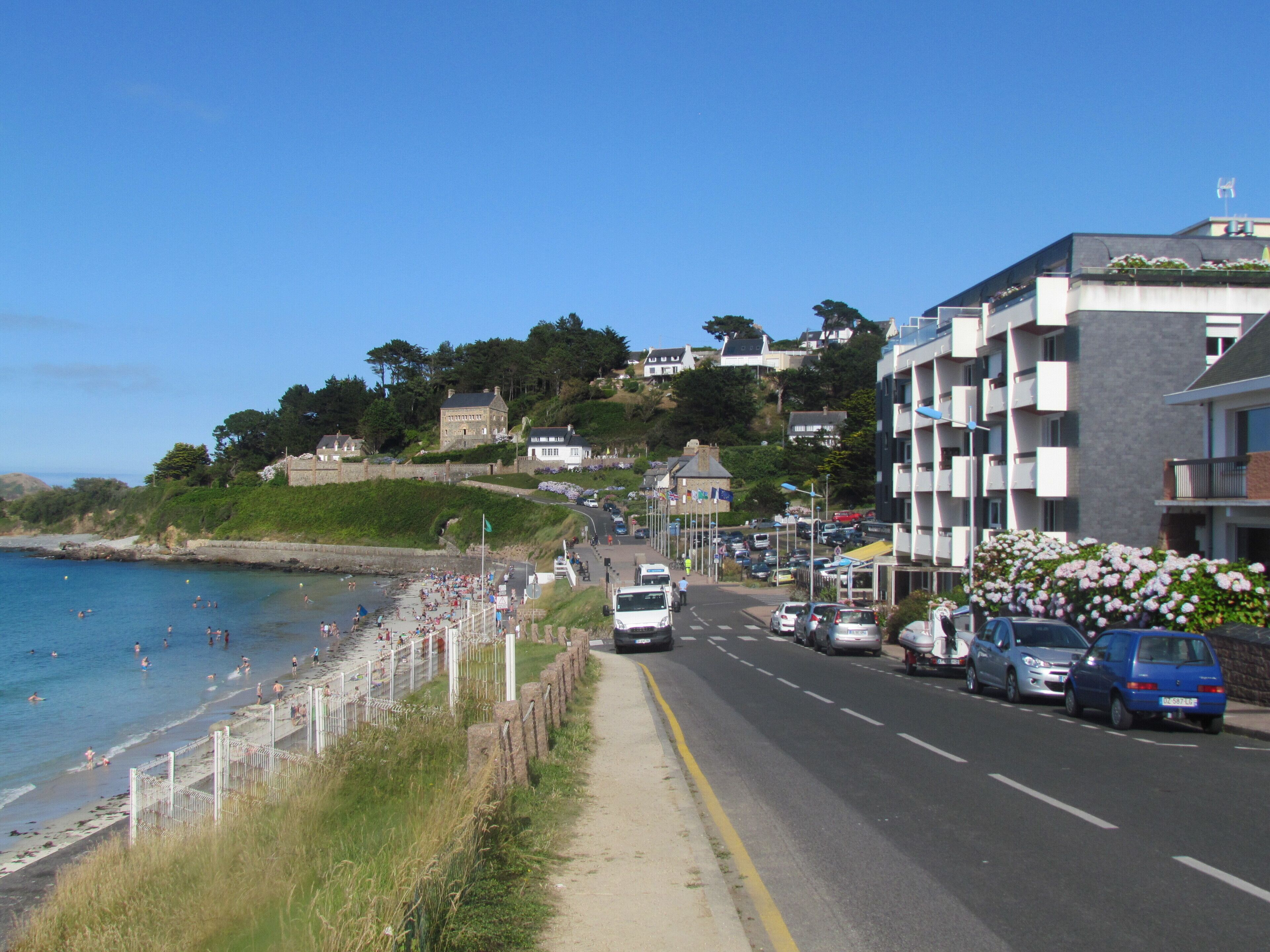 Eine Küstenstraße mit Strand auf der einen Seite und Gebäuden auf der anderen.