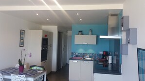 A modern kitchen with white cabinets, a blue accent wall, and a dining area with a table and chairs. - LES PIEDS DANS L'EAU sea at 15 meters PANORAMIC VIEW PERROS GUIREC (PERROS GUIREC)