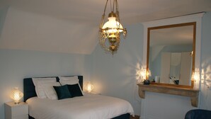 Et soveværelse med seng, sengeborde med lamper, et spejl og en hængende lampe.