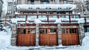 Ein zweistöckiges Gebäude mit einer Stein-Fassade, Holztoren zur Garage und einem Balkon mit Schnee.
