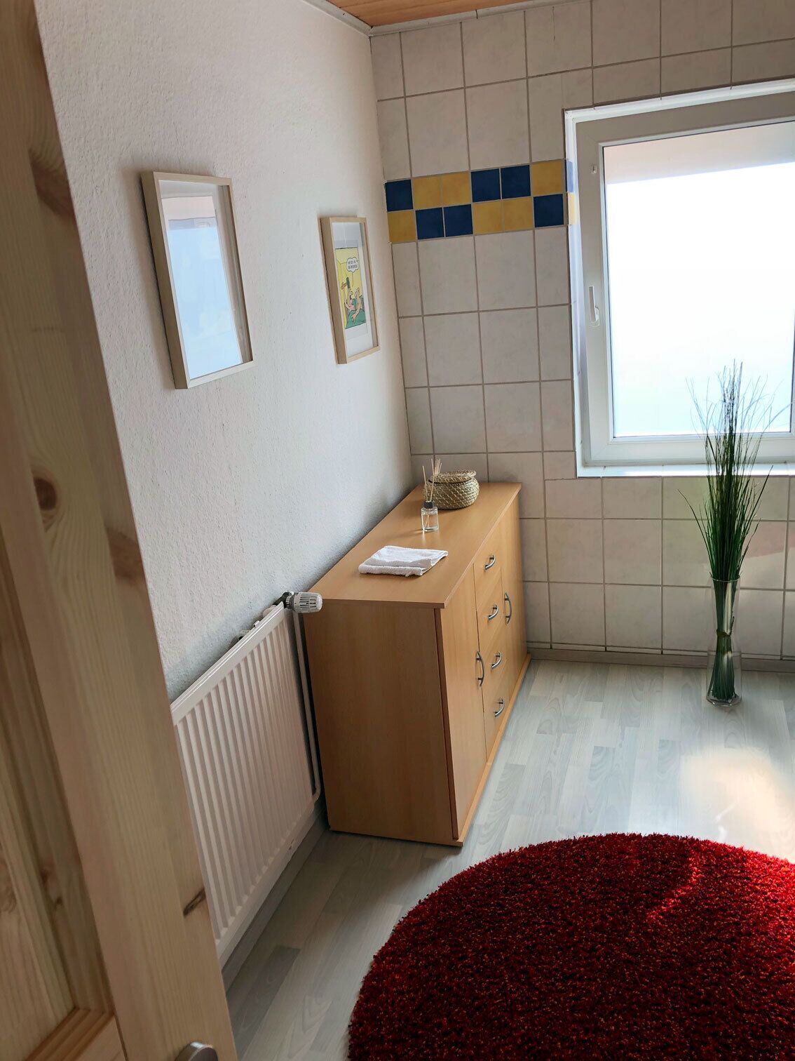 Ein Zimmer mit einem Holzschrank, einem Heizkörper, einem Fenster mit Blick und einem roten Teppich.