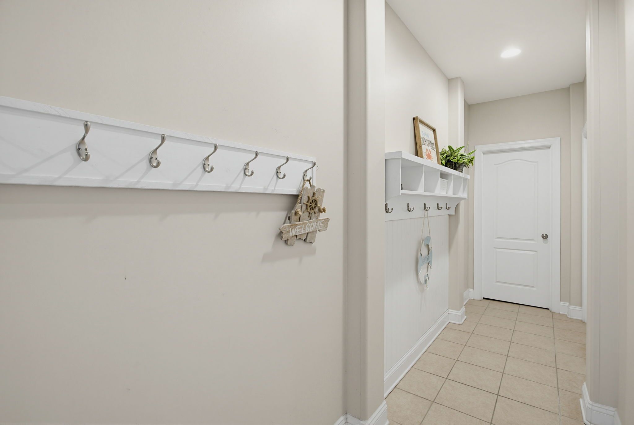 A hallway with a coat rack, a welcome sign, and a shelf with plants.