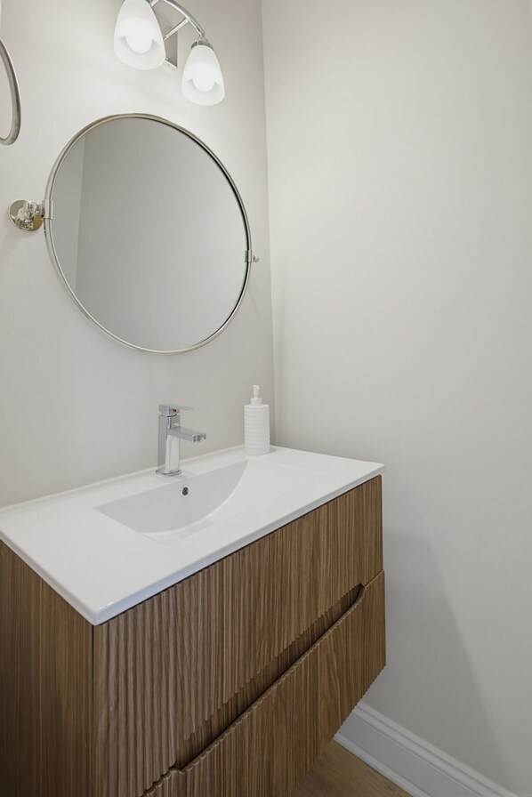 A bathroom with a round mirror, a white sink, a wooden vanity, and a wall-mounted light fixture. - RENOVATED FOR SUMMER 2026.
Oceanfront complex with pool. NOW WITH EV CHARGE. (Surf City)