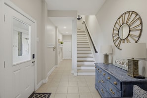 A hallway with a white door, a staircase, a blue dresser with knobs, and a wall-mounted mirror.