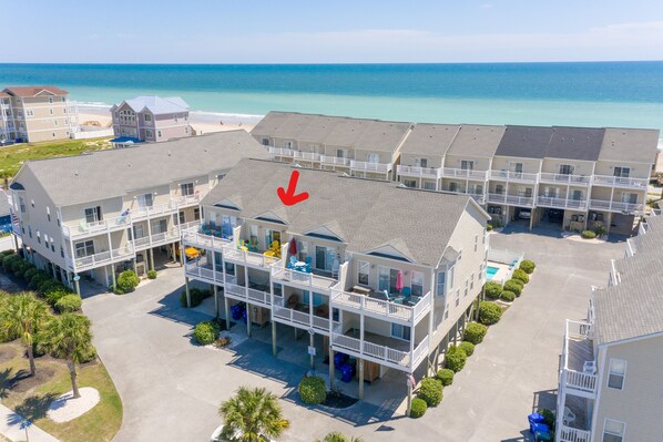 Un hotel frente a la playa con varios balcones, una piscina y vista al océano.