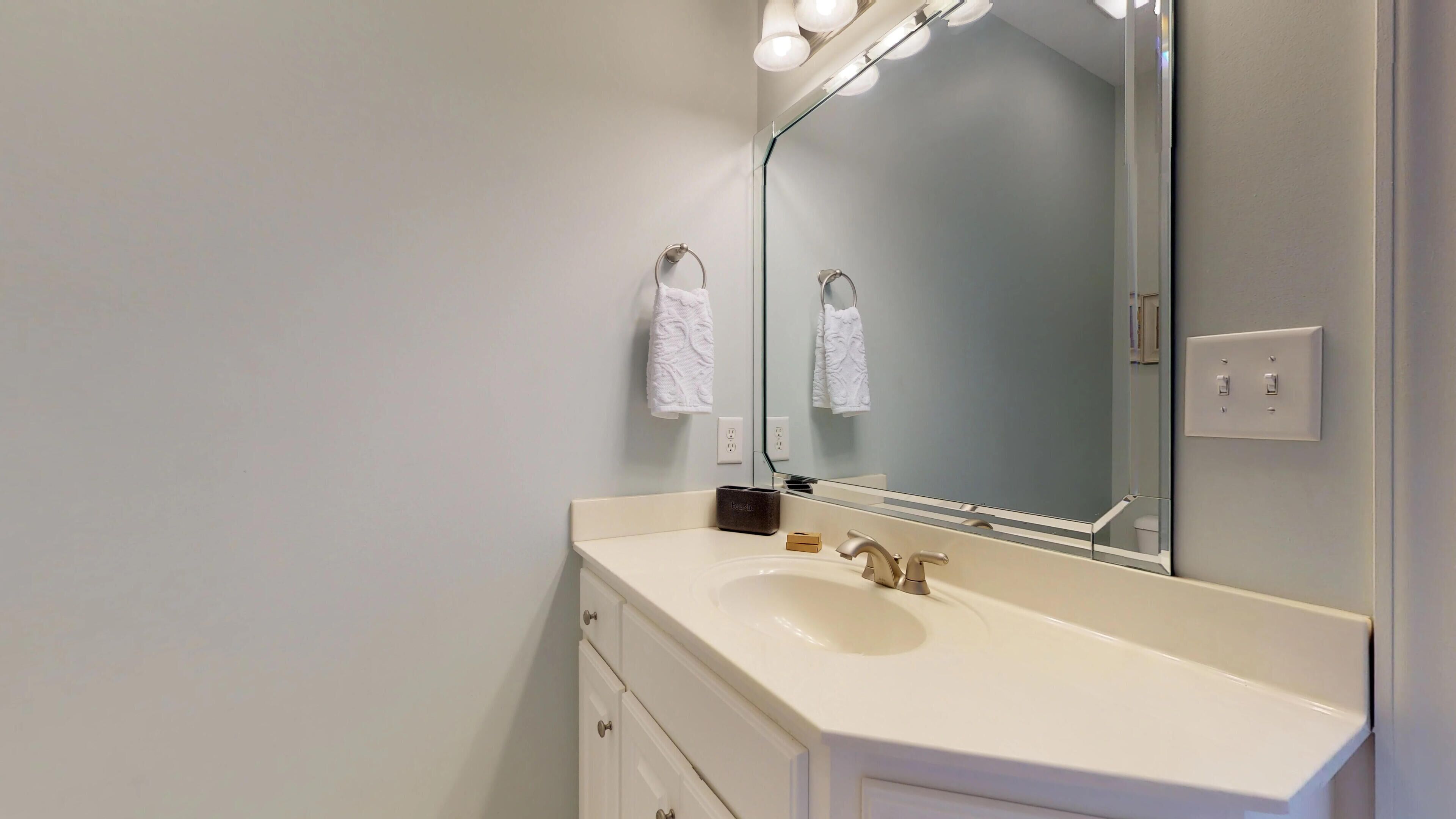 Une salle de bain avec un lavabo blanc, un miroir avec éclairage intégré et un porte-serviettes.