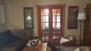 Una sala de estar con un sofá, dos sillones, una mesa de centro con flores y un comedor visible a través de un vidrio.