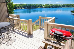 Une terrasse en bois avec un barbecue, une table et des chaises, et une vue sur un lac.